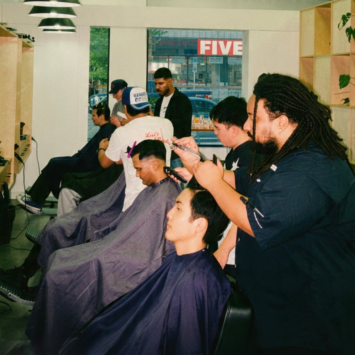 Barbers at Denim & Smith Barbershops cutting clients' hair in a busy, modern barbershop