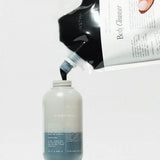 Hand pouring a liquid from a large container labeled 'Firastha' into a smaller bottle on a white background.