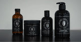 Four grooming products from Global Grooming are lined up on a dark surface against a light gray background. The set includes an amber glass bottle, a black jar of shave cream, a black bottle of shaving soap, and a large black pump bottle of shaving lotion.